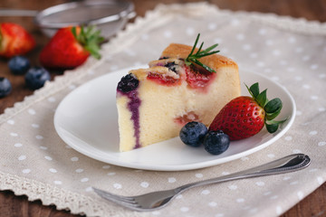 Mixed berry butter cake with fresh blueberries and strawberries on white plate put on wood table in side view copy space. Delicious and moist with sweet and sour taste in homemade bakery concept.