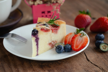 Mixed berry butter cake with fresh blueberries and strawberries on white plate put on wood table in side view copy space. Delicious and moist with sweet and sour taste in homemade bakery concept.
