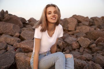 Portrait of a cute girl sitting on the rocks at sunset. 