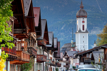 Row of traditional German houses with wooden balconies in historic center of Garmisch with Parish Church St. Martin and Wank mountain in background, Garmisch-Partenkirchen Bavaria Germany Europe - obrazy, fototapety, plakaty