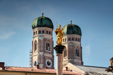Fototapeta na wymiar Two towers of Gothic Frauenkirche cathedral and Mariensaule statue, symbols of Bavarian capital, rise above roofs of Marienplatz square in Altstadt historic center of Munchen, Bayern Germany Europe