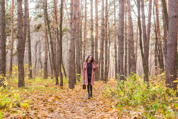 Fototapeta premium Autumn, fashion, people concept - woman with brown retro suitcase walking through the autumn park and smiling