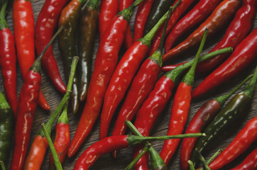 a close-up of a group of red chili peppers on a wooden surface. Some of the peppers are green.