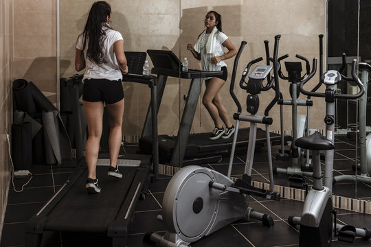 Mujer joven entrenado en la cinta de correr en el gimnasio con camiseta blanca y pantal&oacute;n corto negro