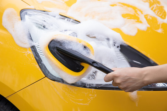 Sponge Washer Cleaning Headlights Of A Yellow Car