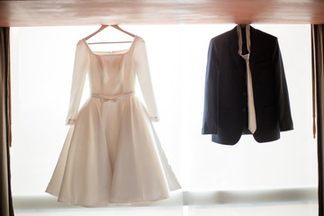 Groom suit and bride dress hanging on the window prepare to use on wedding ceremony day. sign of wedding ceremony.
