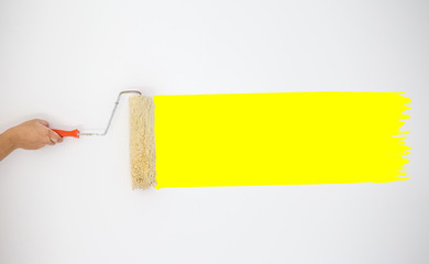 Painter's hand held roller to painting yellow color paints on the grey wall. image for add text, background, wallpaper, objects, copy space,article and illustration.