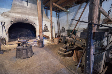 Fototapeta na wymiar Interior of the old mediaeval vintage water powered blacksmith workshop or forge with hammer, anvil, tools and furnace, old technology still working in Czech Republic.