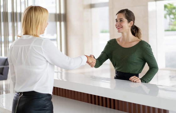 Office Receptionist Greeting Corporate Partner With Handshake. Woman In Formal Clothing Shaking Hands Over Reception Counter. Partnership Concept