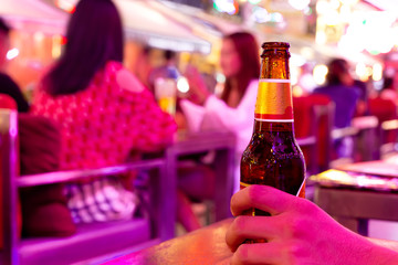 Man hand holding bottle of cold beer in the bar on vacation.