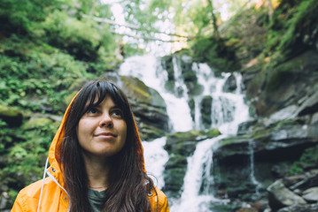 smiling woman in yellow raincoat with waterfall on background