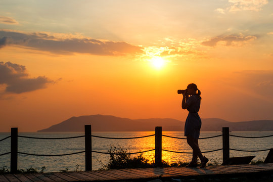 Girl with camera at sunset at sea