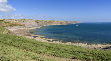 A sweeping bay, on the South Wales coast, as viewed from the Wales Coastal Path. The day is sunny and the water is blue.