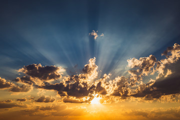 Blue and orange sky background with clouds and rays of sunset sun