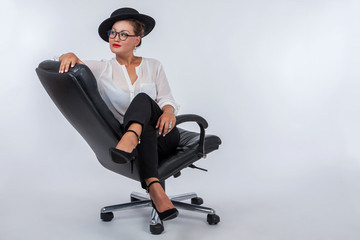 Girl in glasses. A woman is sitting in a black chair. Girl in a white blouse. Asian girl. Asian fashion model. Thoughtful girl. Office chair.