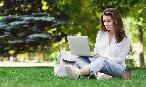 Pretty woman sitting in park and using laptop