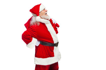 Christmas. Santa Claus is suffering from back pain and holds a red bag with gifts on his back. Isolated on white background.