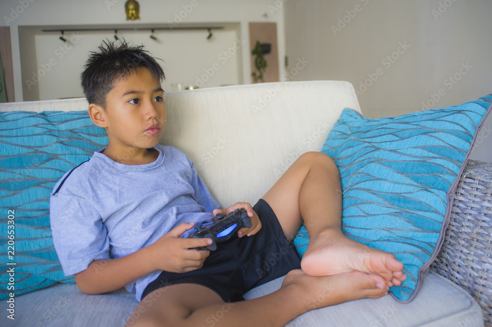 Wall mural  Latin young child 8 years old excited and happy playing video game online holding remote controller enjoying having fun sitting on couch in internet gaming