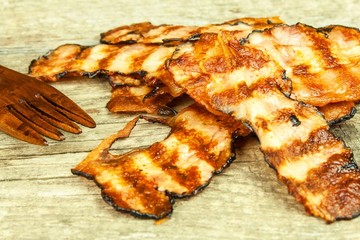 Grilled bacon on white. Crispy Cooked Bacon On Wooden Table. Unhealthy food. Risk of obesity. Homemade barbecue.