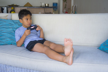  Latin young child 8 years old excited and happy playing video game online holding remote controller enjoying having fun lying on couch in internet gaming