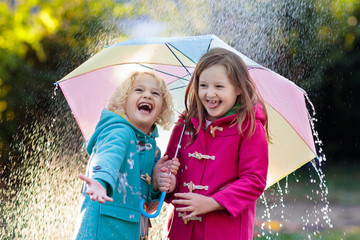 Kids with umbrella playing in autumn shower rain.