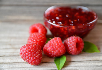 Fresh raspberry jam in a glass bowl and freshly picked raspberries on old wooden background.
Selective focus.