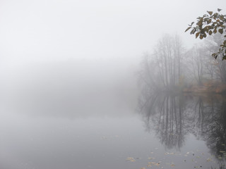 Fototapeta na wymiar Thick dense fog, haze on the river during the late autumn. Misty, cloudy defocused lake. Landscape with morning fog