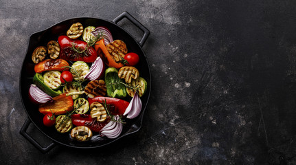 Grilled assorted vegetables in cast iron pan on dark background copy space