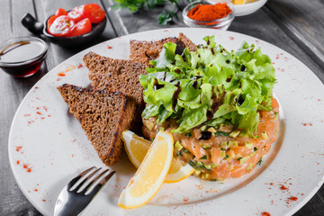Tartar with salmon and avocado decorated with greens on plate on wooden table. Delicious appetizers