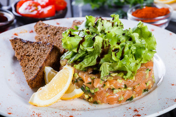Tartar with salmon and avocado decorated with greens on plate on wooden table. Delicious appetizers