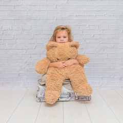 the girl, baby in dress on white brick wall background with suitcase, toy bear