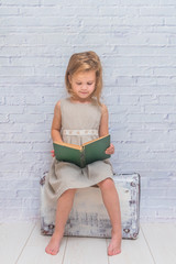 the girl, baby in dress on white brick wall background with suitcase, with a book