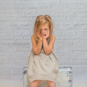 the girl, baby in dress on white brick wall background with suitcase