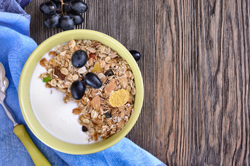 Useful breakfast of muesli with grapes is in a bowl on a wooden table