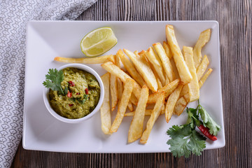 Appetizing guacamole sauce from the avocado pulp on a white plate next to the French fries are ready to be eaten.