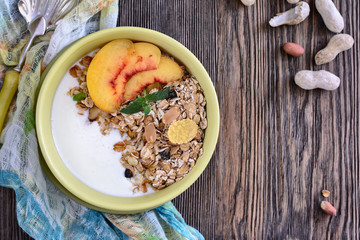 Useful breakfast of muesli with peach slices is in a bowl on a wooden table