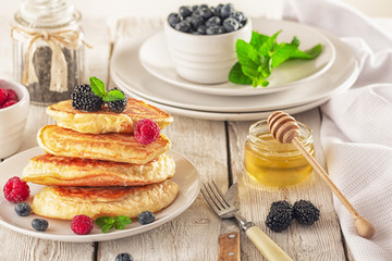 Pancakes with blueberries, honey and raspberry on a wooden background