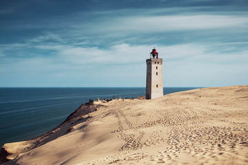 Bright beach sand dunes with the famous danish landmark lighthouse with blue sky background. Rubjerg Knude Lighthouse, L&oslash;nstrup in North Jutland in Denmark, Skagerrak, North Sea