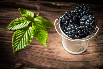 Sweet blackberries in bucket leaf on vintage wooden board