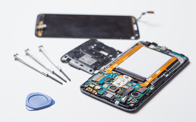 A process of mobile phone repairing and other gadgets parts of disassembled smartphone with screwdrivers on white table.