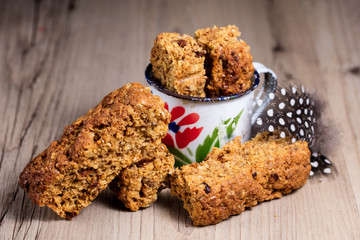 Home-made rusks displayed in a tin cup with a guineafowl feather on a wooden surface