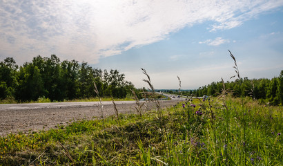 Turn of old country road with moving cars at summer day with field grass in the foreground