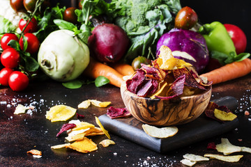 Vegan snacks, multicolored vegetable chips in wooden bowl and set of fresh farmer vegetables,...