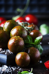 Brown cherry tomatoes with sea salt and green basil on dark table, autumn harvest, selective focus