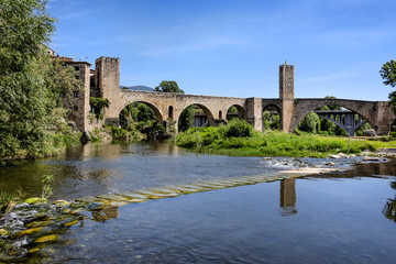 Fototapeta na wymiar Spain, Catalonia, Besalu: Panorama view on the famous skyline of old ancient fortified Spanish town with medieval bridge, river El Fluvia, tower, houses, green trees and blue sky in the background.