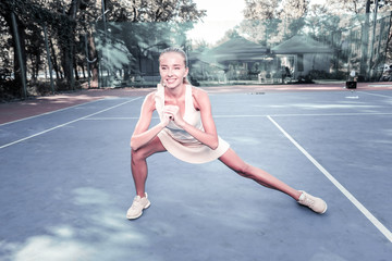 Fototapeta na wymiar On court. Joyful female player grinning and stretching