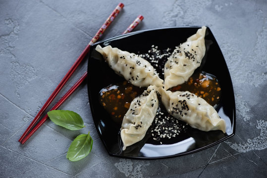 Black plate with steamed korean dumplings, sesame and dipping sauce, high angle view on a grey concrete background, horizontal shot