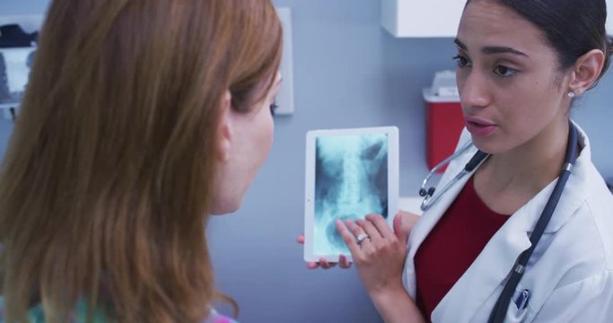 Close up of lovely latina doctor holding tablet to review patients hip x ray