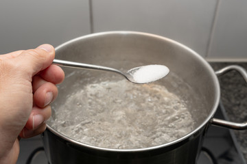 Löffel in der Hand mit Salz über kochendem Wasser im Topf
