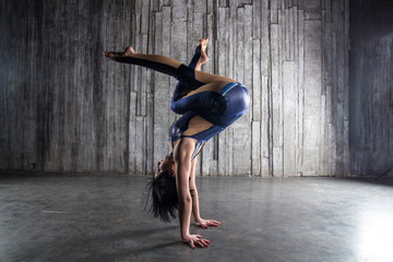 Young very flexible female acrobat standing on hand over gray background in photo studio